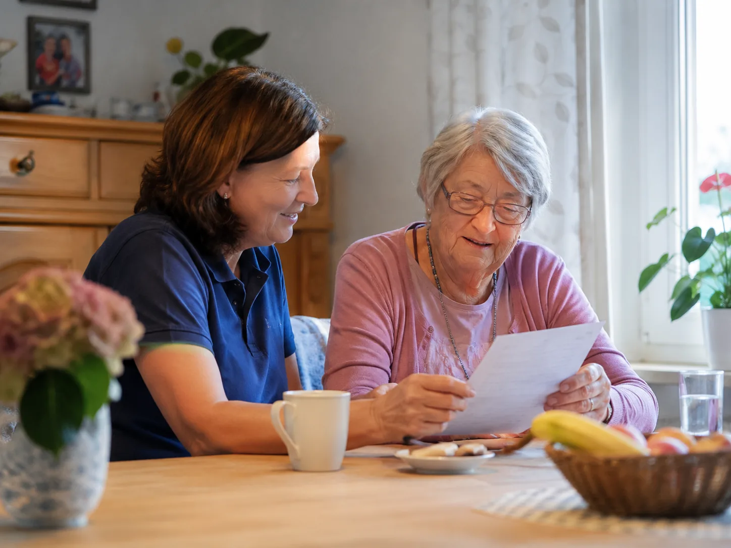 Pflegekraft und ältere Dame lesen gemeinsam ein Dokument